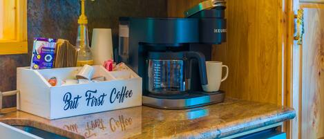 A kitchen counter with a coffee maker, a box labeled "But First Coffee," and a coffee cup.