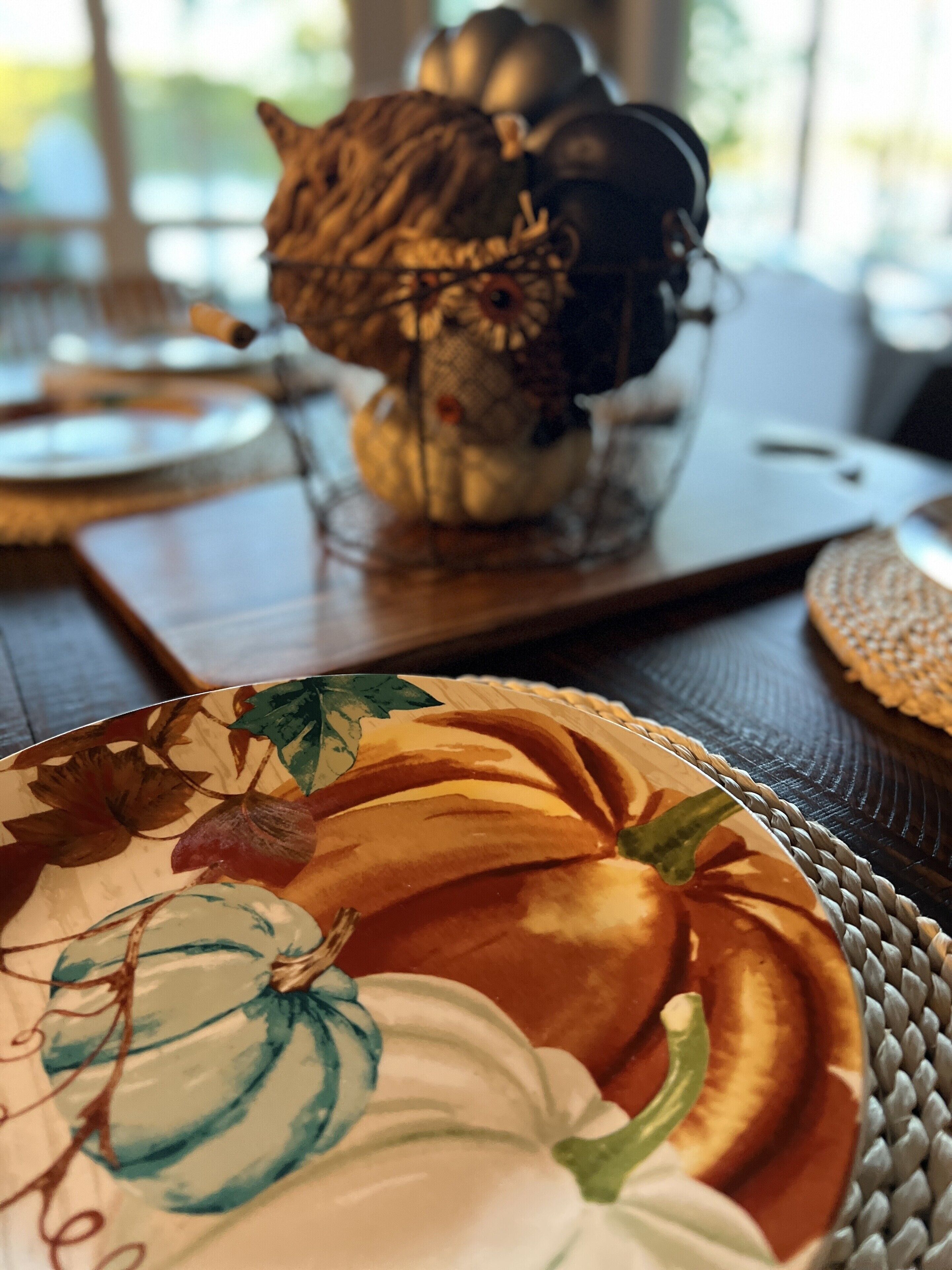 A table setting with a decorative pumpkin centerpiece, a woven placemat, and a patterned plate.