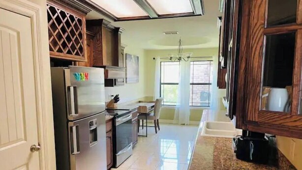 A kitchen with a refrigerator, stove, and microwave. There is a window with curtains and a chandelier. - Sundown Stay (San Juan)