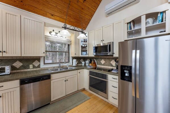 A modern kitchen with white cabinets, stainless steel appliances, and a wooden ceiling.