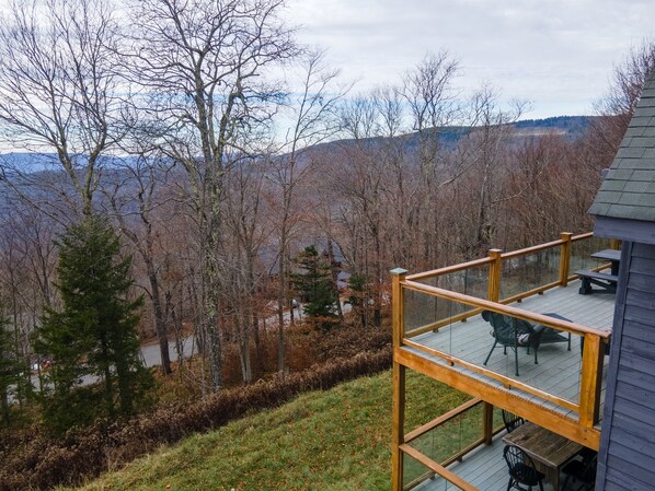 A deck with outdoor furniture, overlooking a forested area and distant mountains.