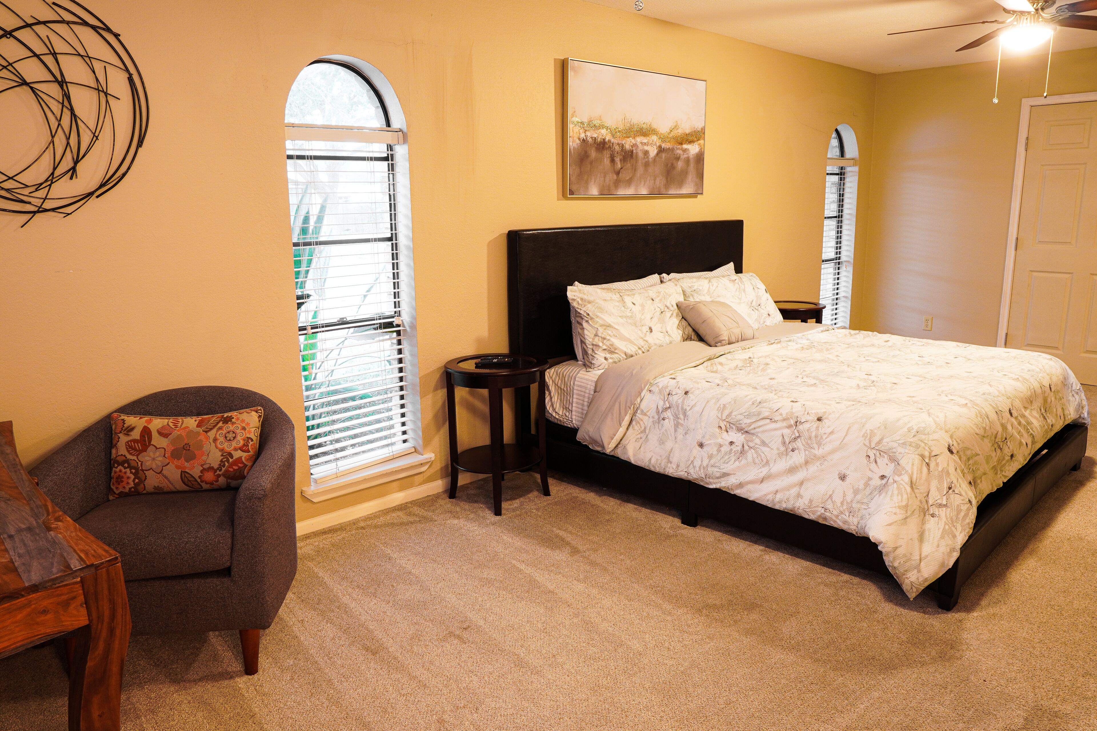 A bedroom with a bed, a chair, a nightstand, a window with blinds, and a ceiling fan.
