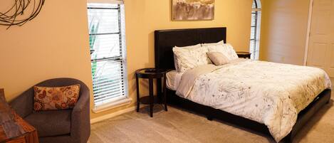 A bedroom with a bed, a chair, a nightstand, a window with blinds, and a ceiling fan.