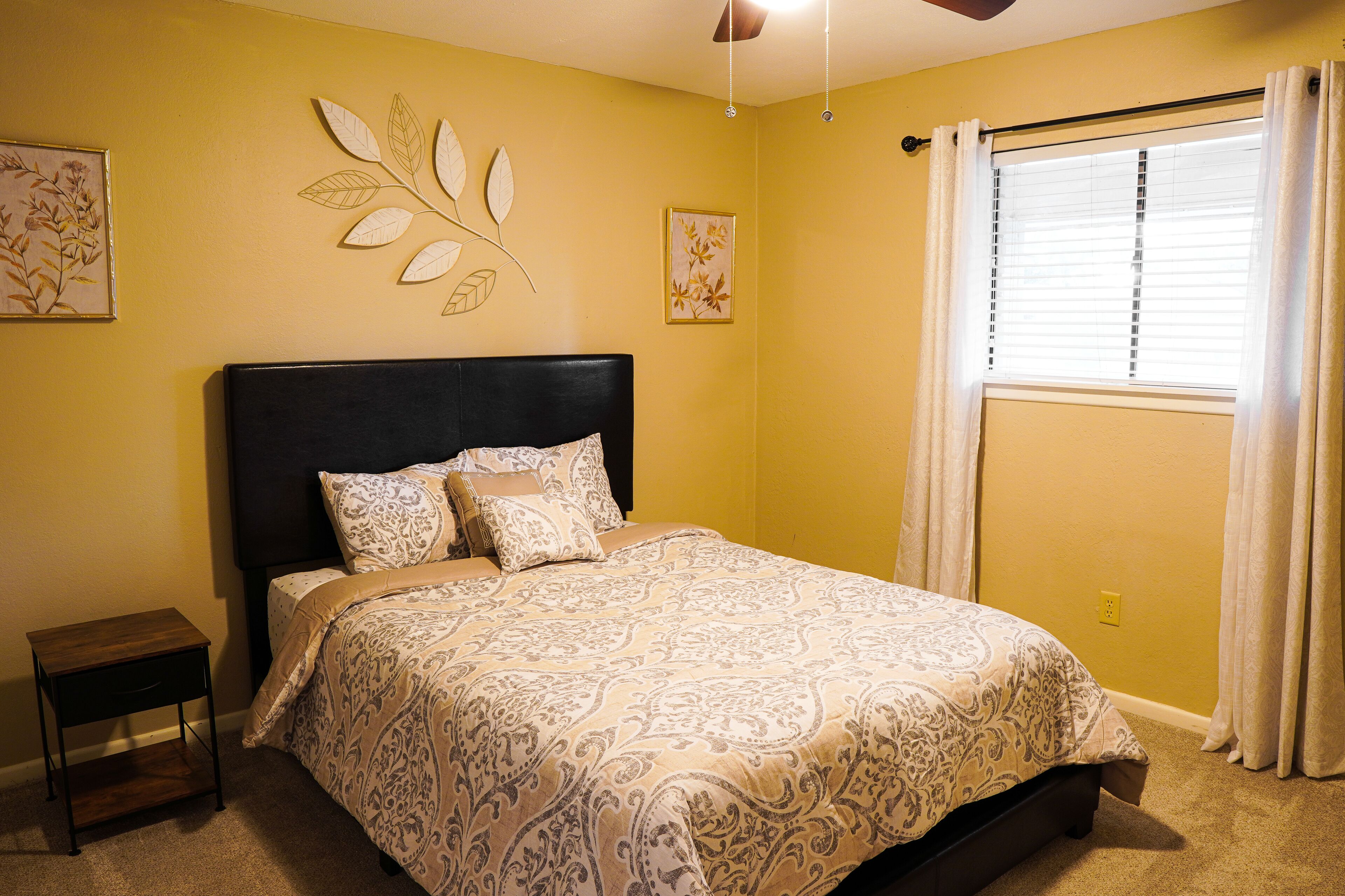 A bedroom with a bed, a nightstand, and a window with curtains.