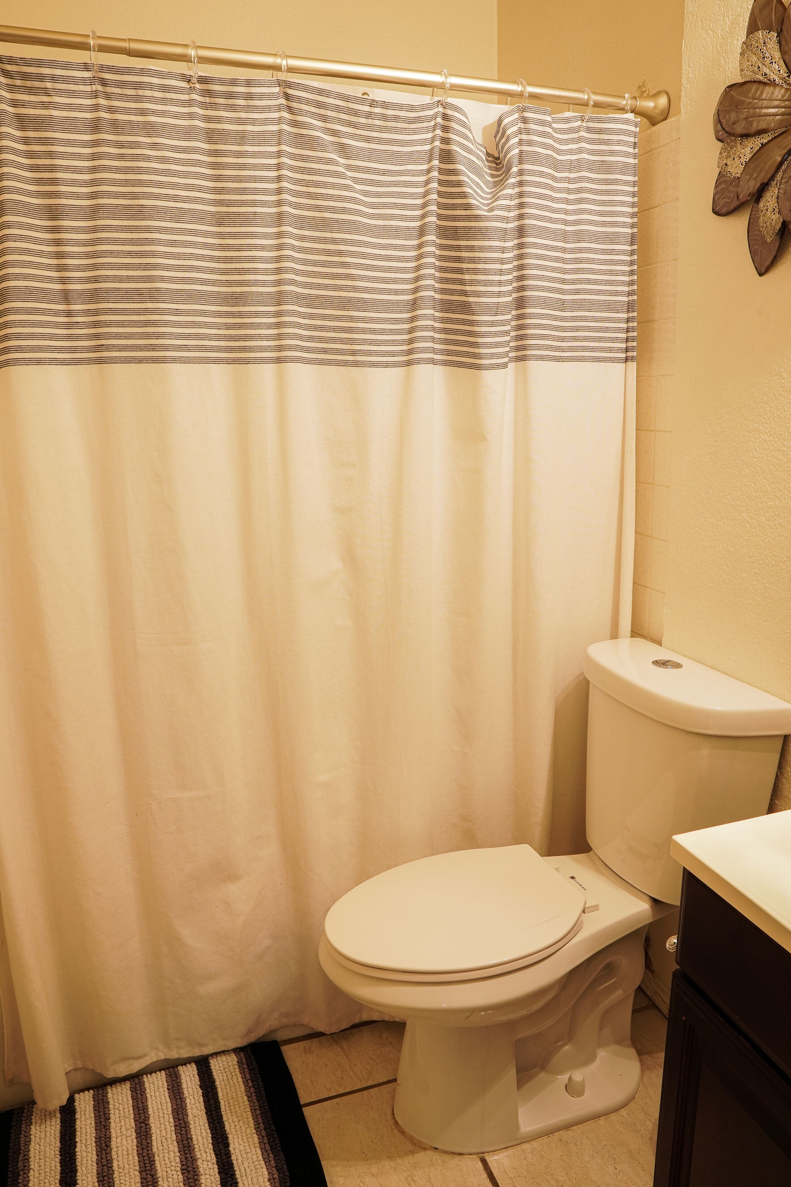 A bathroom with a striped shower curtain, a white toilet, and a small rug on the floor.