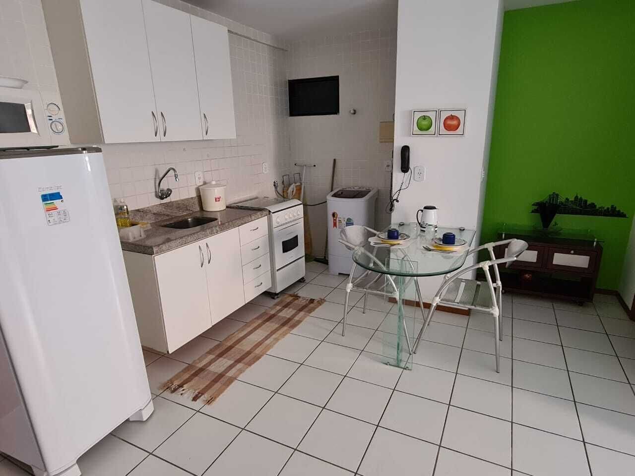 A compact kitchen with white cabinets, a refrigerator, a microwave, and a small dining area with a glass table and chairs.