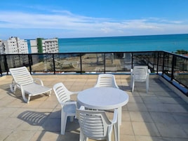Terraço com mesa e cadeiras, com vista para um corpo de água e edifícios.