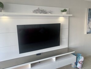 Ett modernt vardagsrum med en platt-TV som är monterad på en vit vägg, en liten hylla med dekorativa föremål och ett klinkergolv.