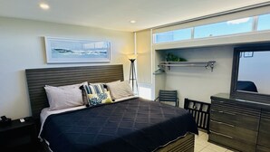 Un dormitorio moderno con una cama grande, un escritorio y una silla. Hay una ventana sobre el escritorio y un cuadro en la pared.