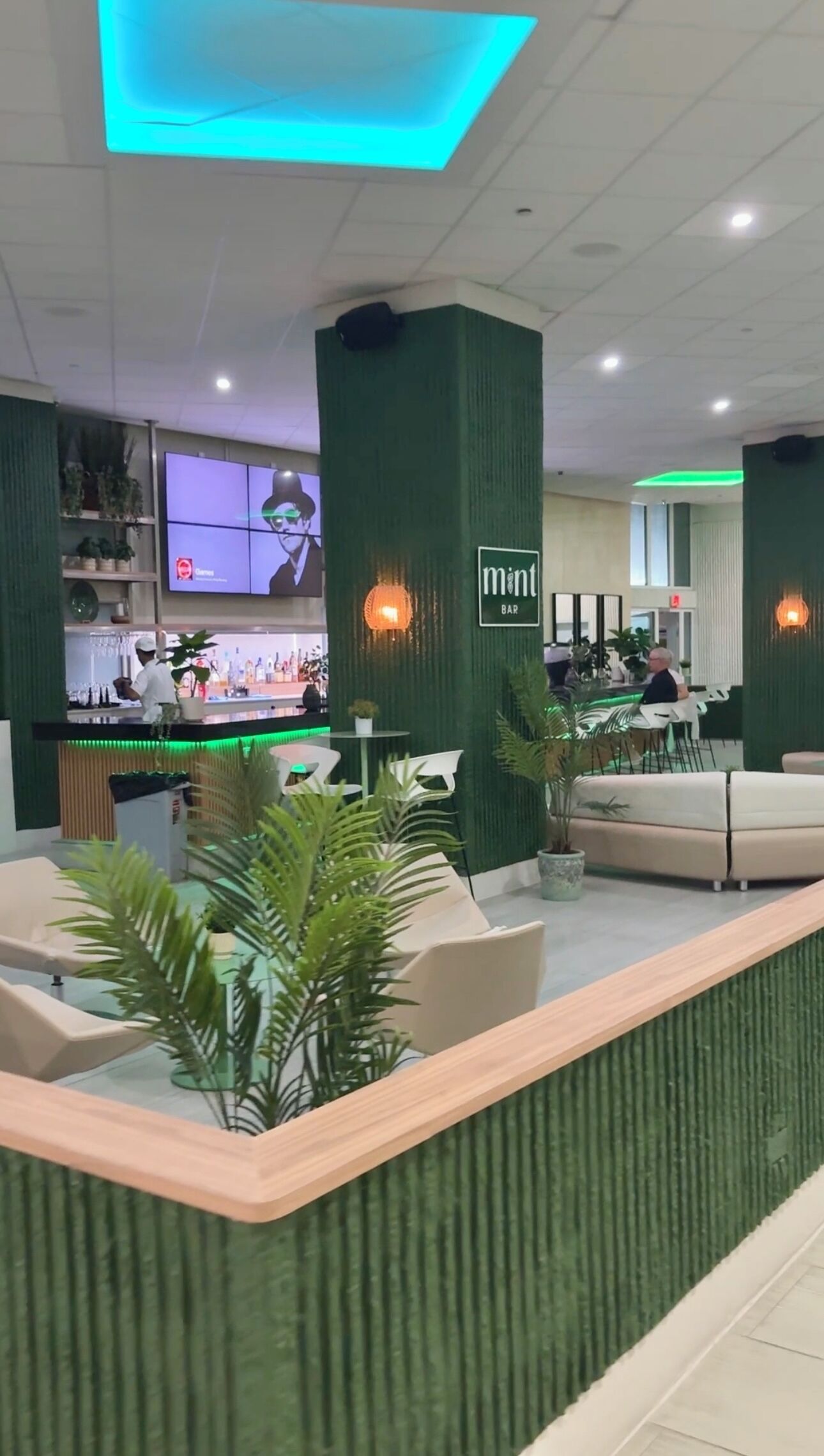 Een moderne bar met groene accenten, zitplaatsen en een bartender die drankjes bereidt.