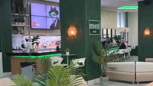 Zona de bar moderna con detalles en verde, asientos y un barman preparando bebidas.