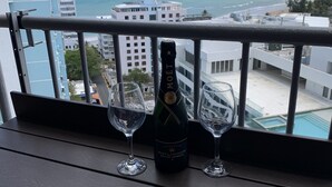 Un balcón con una botella de Moët & Chandon y dos copas sobre un repisa de madera, con vistas a la costa, edificios y un cielo despejado.