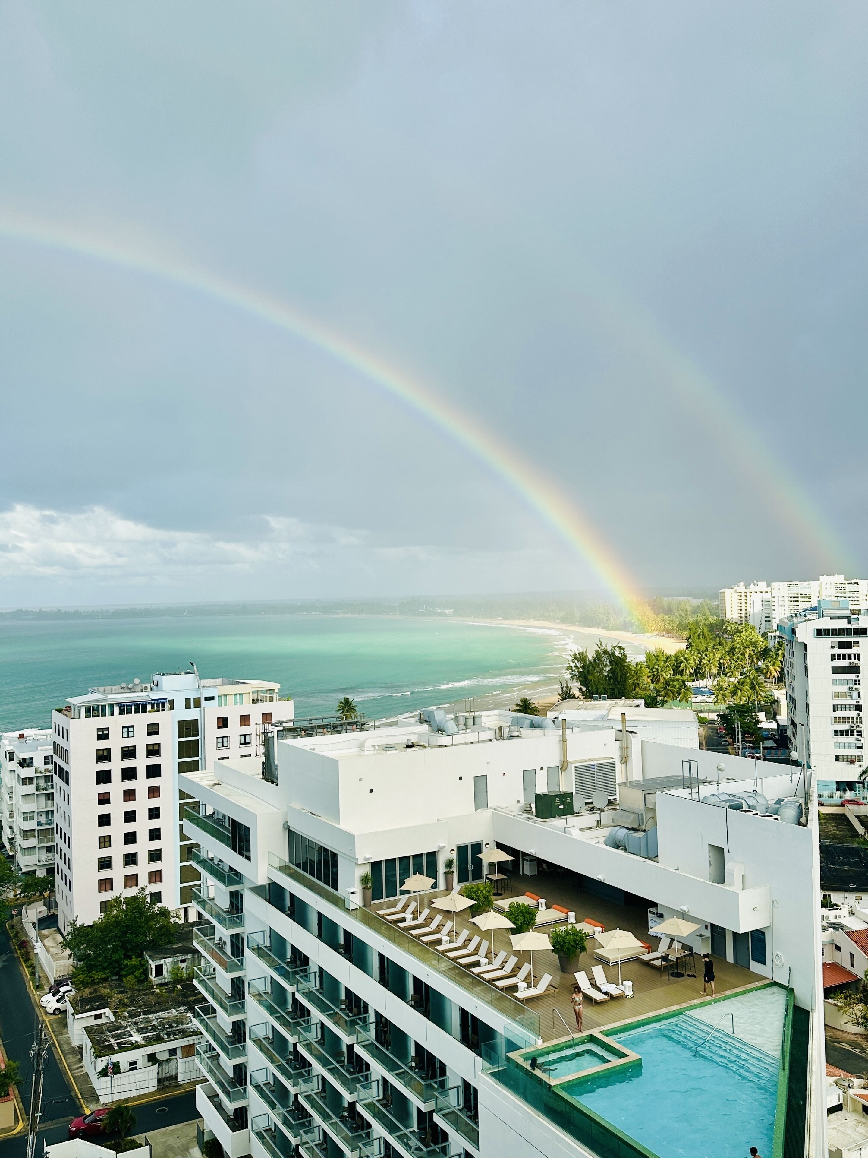 Een hotel met een zwembad op het dak, uitzicht op het strand en een regenboog.