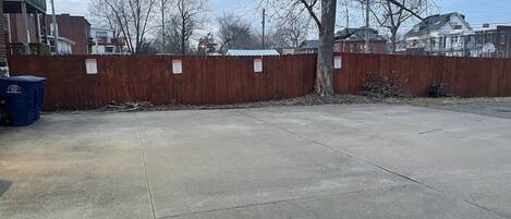A concrete parking lot with a wooden fence and leafless trees.