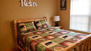 A bed with a wooden frame and a quilt with a bear pattern, a lamp, and a window with blinds. - 2 Bedroom  Cabin inside Pigeon Forge (Pigeon Forge)
