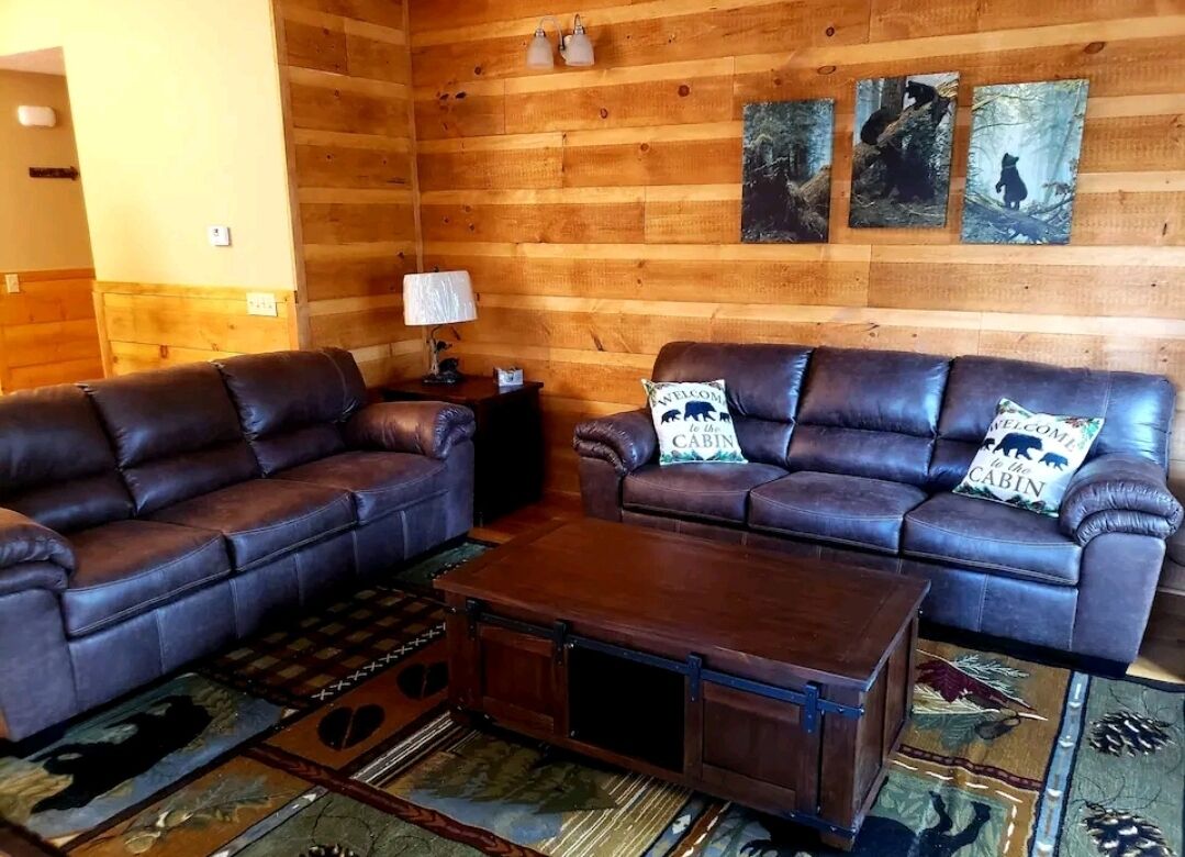A log cabin interior with two leather sofas, a wooden coffee table, and a rug with animal prints.