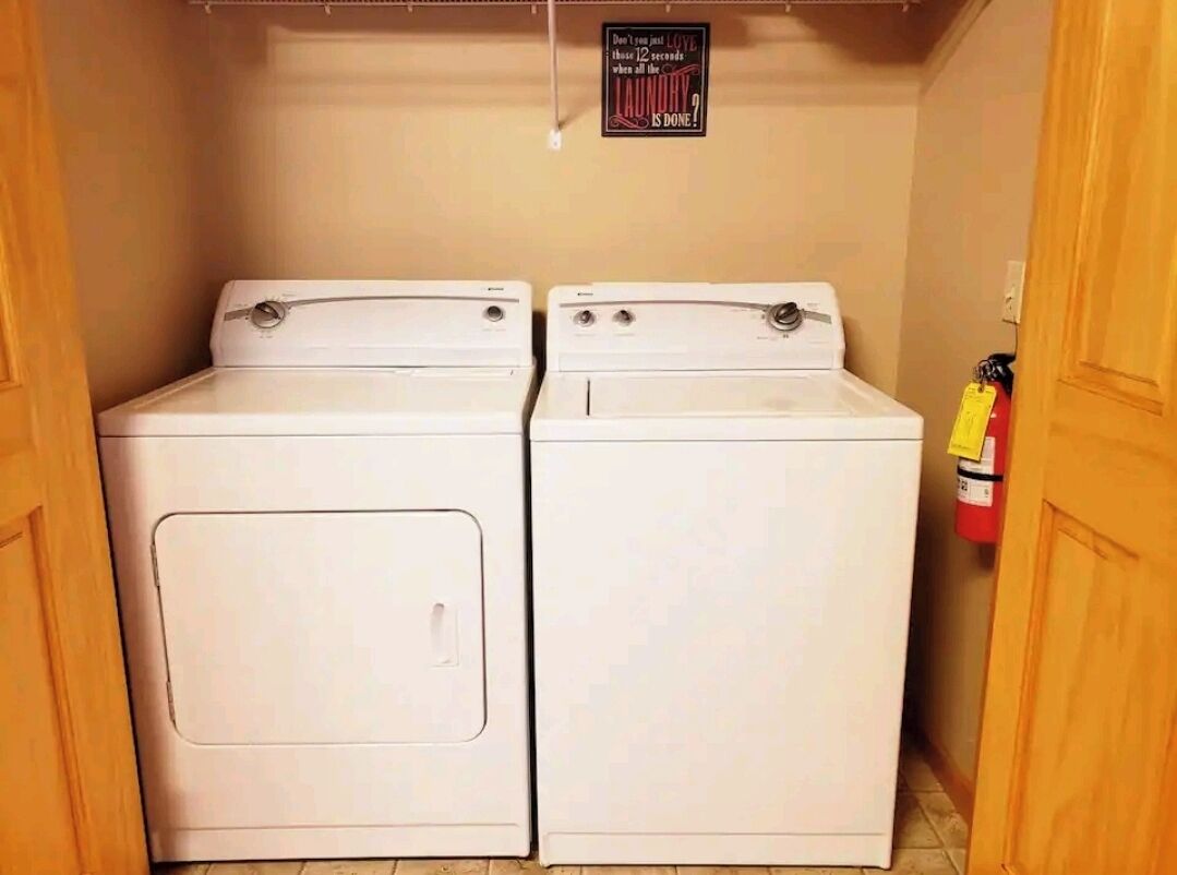 A laundry room with two white front-loading washers and dryers, a fire extinguisher on the wall, and a sign above the dryers.