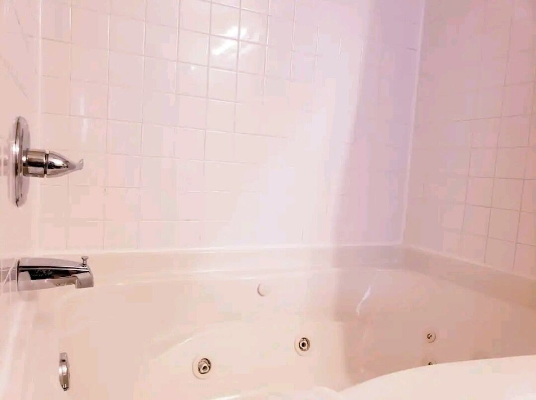 A bathroom with a white bathtub, chrome fixtures, and white tiled walls.