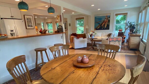Un comedor espacioso con una mesa y sillas de madera, una cocina al fondo y un gran ventanal que aporta luz natural.