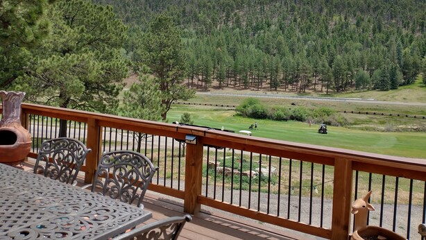 Une terrasse en bois avec des chaises et une table en métal, offrant une vue sur un terrain de golf et des collines boisées.