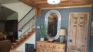 Un escalier en bois avec une rampe noire, une console en bois surmontée d’un miroir, une lampe et une porte décorative.