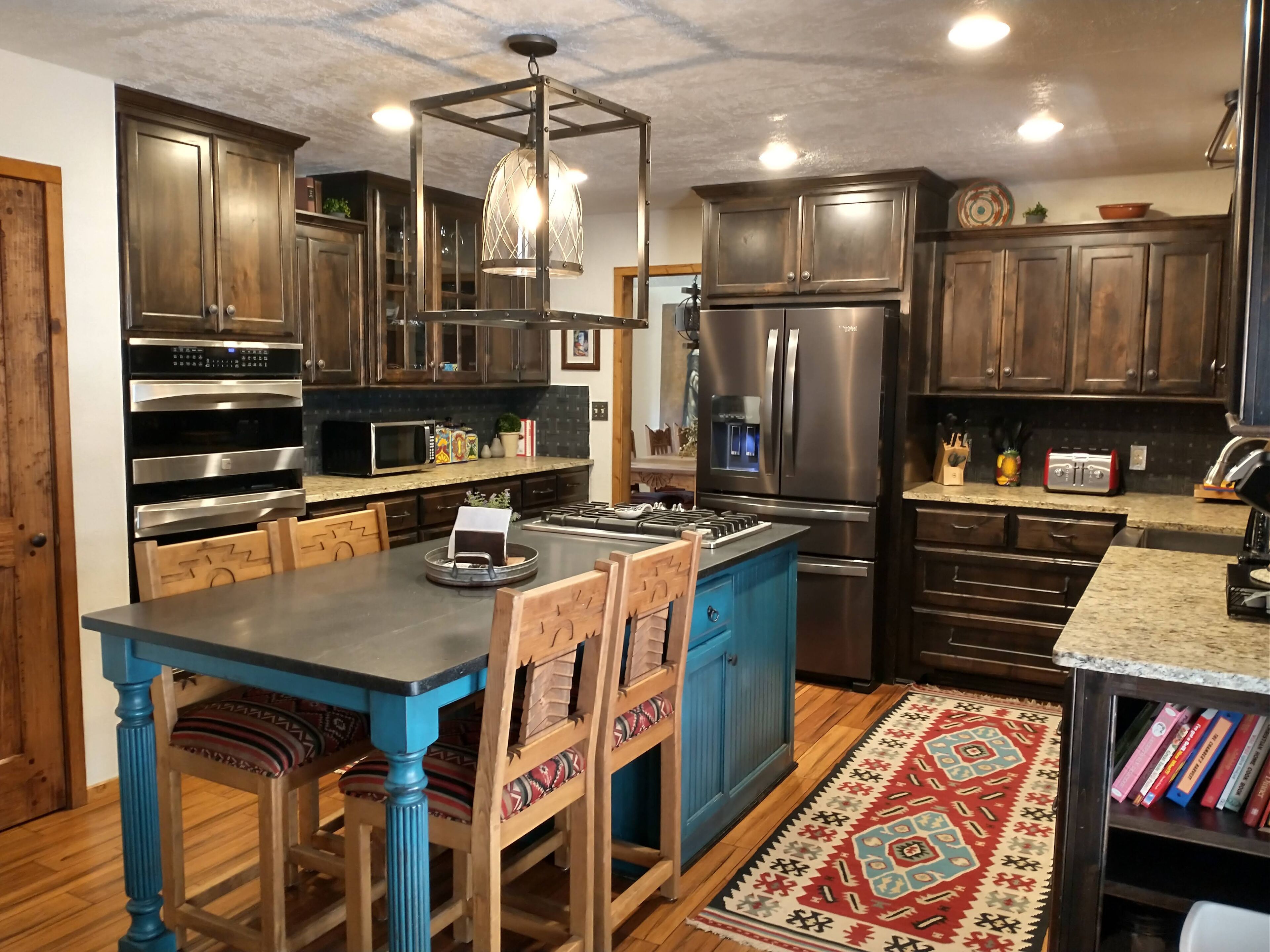 Une cuisine moderne avec des meubles de couleur bois foncé, des appareils en acier inoxydable, un îlot central bleu et un tapis à motifs.
