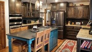 Une cuisine moderne avec des meubles de couleur bois foncé, des appareils en acier inoxydable, un îlot central bleu et un tapis à motifs.