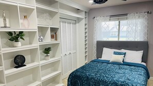 Une chambre à coucher avec un lit, une grande étagère blanche et une fenêtre avec des rideaux.
