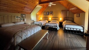 Une chambre mansardée chaleureuse avec trois lits, des poutres en bois et un plafond en pente.