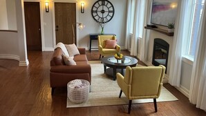 Una sala de estar con un sofá marrón, sillones amarillos, una mesa de centro redonda y un reloj de pared grande.