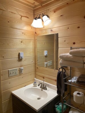 Un baño con paneles de madera, un lavabo, espejo, toallero y repisa con artículos de aseo.