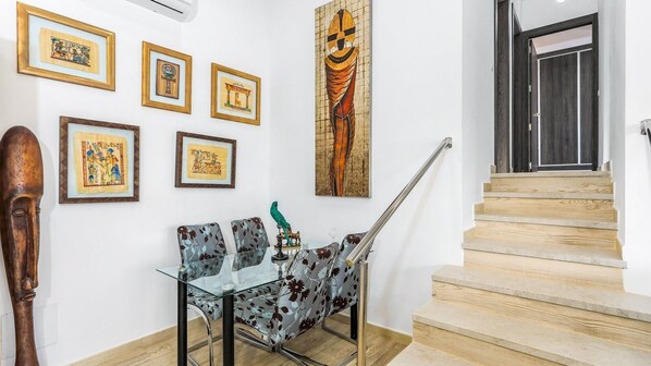 Un comedor con una mesa de vidrio, sillas con motivos florales y cuadros en la pared.