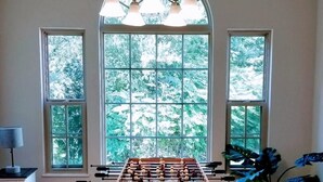 Una habitación con mesa de fútbol, ventanas amplias con vista a árboles y una lámpara colgante.