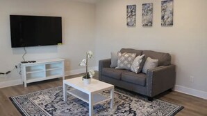 Ein Wohnzimmer mit grauem Sofa, weißem Couchtisch, Flachbildfernseher und einem dekorativen Teppich.