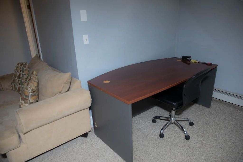 A room with a beige sofa, a wooden desk, and a black office chair.