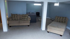 Una habitación con un sofá color beige, un pequeño otoman, un escritorio y una silla.