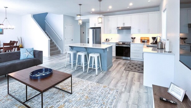 Une cuisine moderne avec des meubles blancs, un îlot central doté de tabourets et un escalier menant à un autre niveau.