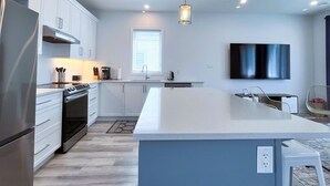 Une cuisine moderne avec des armoires blanches, un grand îlot central, des appareils en acier inoxydable et des luminaires suspendus.