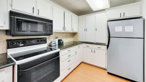 Una cocina moderna con armarios blancos, un microondas negro, un refrigerador de acero inoxidable y un horno empotrado.