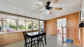 Un comedor con una mesa y sillas de madera, un ventilador de techo y ventanas amplias que ofrecen vistas al exterior.