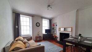 A living room with a sofa, a fireplace, a TV, and a dining area with a table and chairs. - Lovely 2 Bedroom Flat in the Heart of the City (Edinburgh)