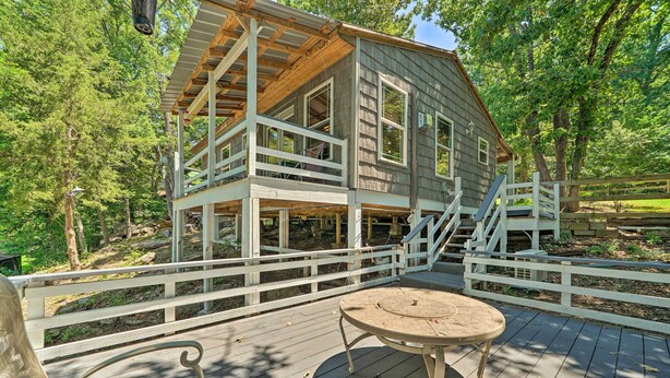Eine Holzhütte mit Balkon, Tisch und Stuhl auf einer Terrasse, umgeben von Bäumen.