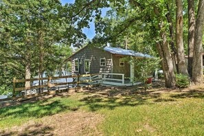 Un chalet rustique doté d’une terrasse en bois, entouré d’arbres et bordé par un lac.
