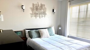 Et soveværelse med en seng, et skrivebord og en vægmonteret lampe.