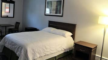 A hotel room with a large bed, a desk, a chair, a nightstand, and a lamp.