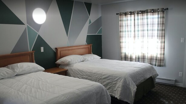 Habitación de hotel con dos camas individuales, cabecera de madera, mesita de noche, ventana con cortinas a cuadros y pared con un diseño geométrico.