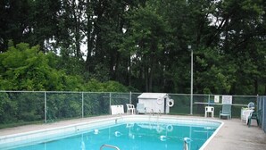 Una piscina rectangular con una escalera metálica, rodeada por una cerca de malla.