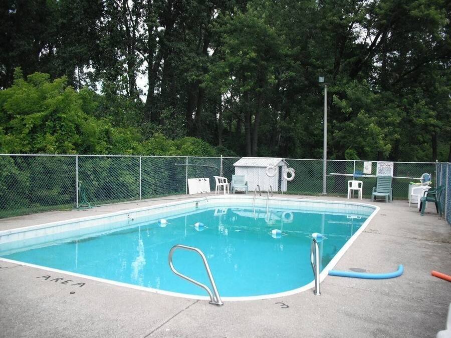 Una piscina rectangular con una escalera metálica, rodeada por una cerca de malla.