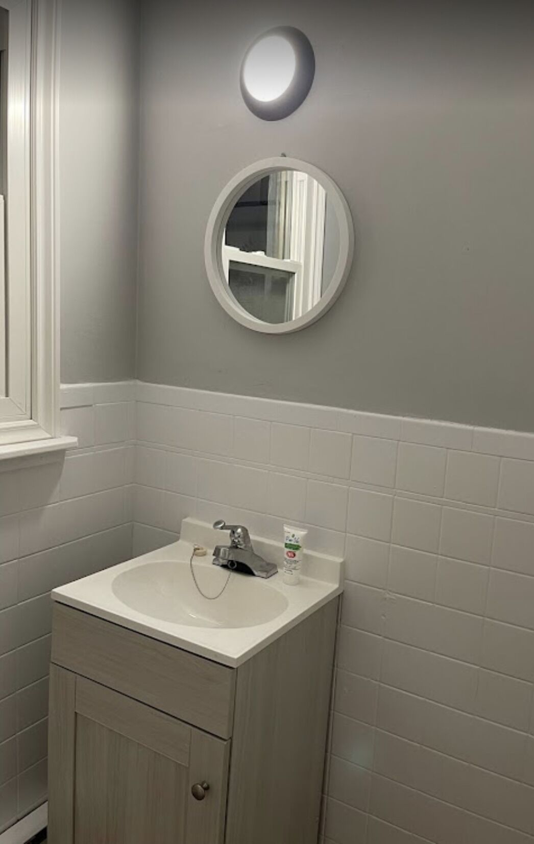A bathroom with a white sink, a mirror, and a round light fixture on the wall.