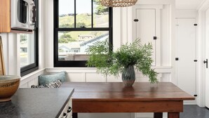 A kitchen with a wooden table, bench, and hanging light fixture. - Historic Beach Cottage with Ocean View Deck - Steps to Beach (Dillon Beach)